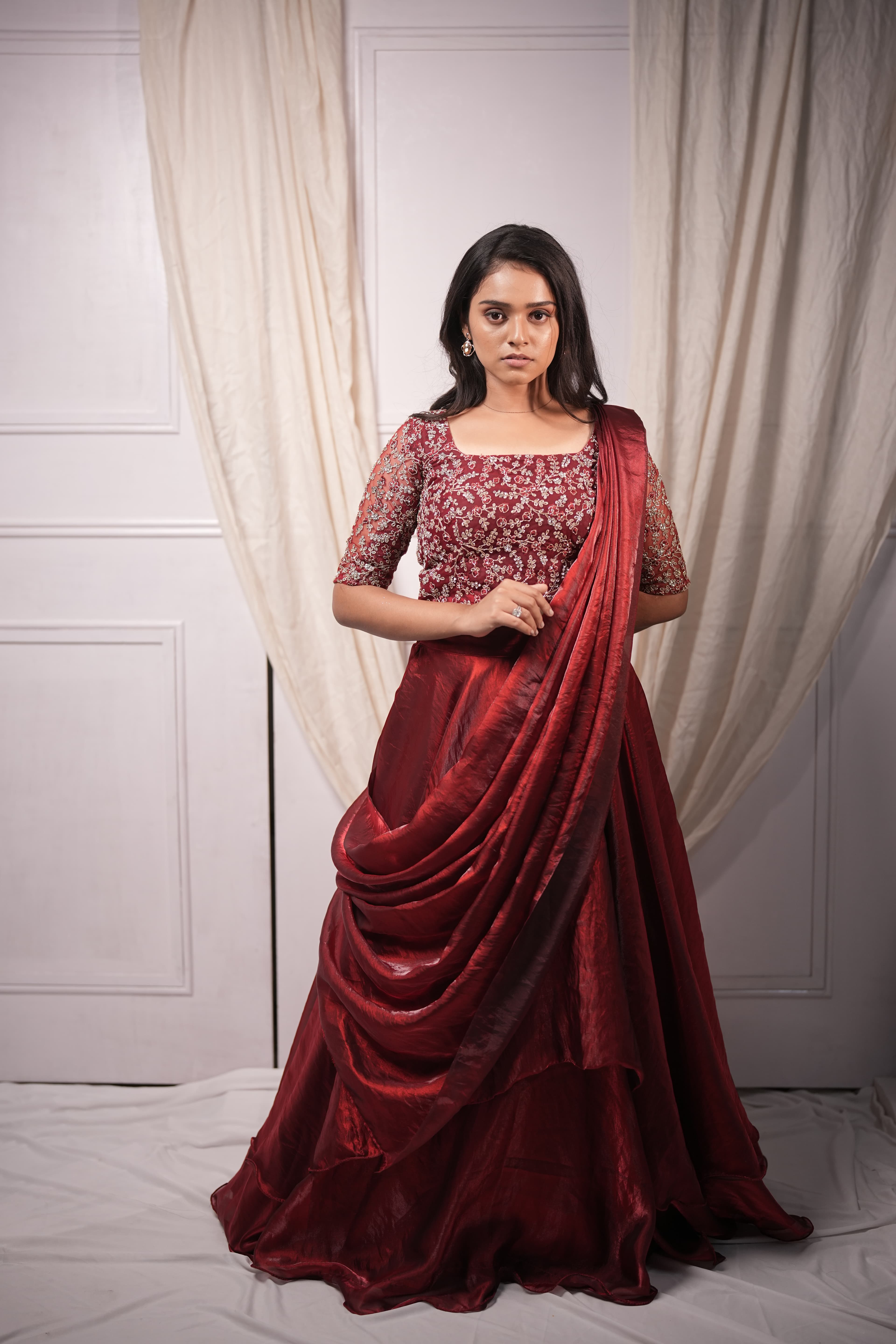 Bride in a maroon Kanjivaram silk drape with gold zari, soft curtain backdrop